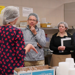 Four people listen to a dietician speak about the Nutrition Department while a employee preps food