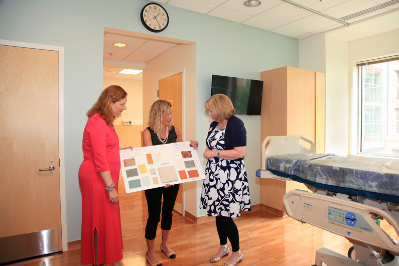 While standing in a hospice suite room, NIH staff hold up a design poster board and review the color scheme and design elements of the new care units