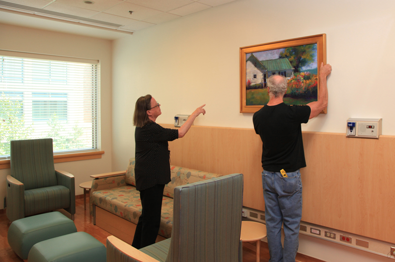 Woman points to artwork that is being hung on the wall by a man