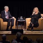 Dr. Francis Collins, director of the NIH sties in a chair to the left. Barbra Streisand holds a microphone and sits in a chair to the right – speaks to the audience
